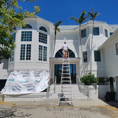 Eco-Friendly-Roof-Cleaning-Coveed-Plants Man on ladder pressure washing roof and Covered up Plants